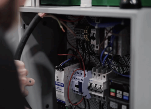 Close up of technician inspecting internal components of a control panel during equipment testing.